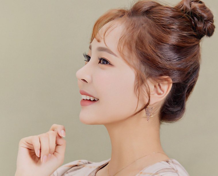 손을 턱 가까이 든 채 웃는 올림머리 모델 옆모습(베이지 배경)